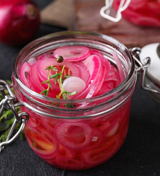 A jar of pickled red onions on a dark background