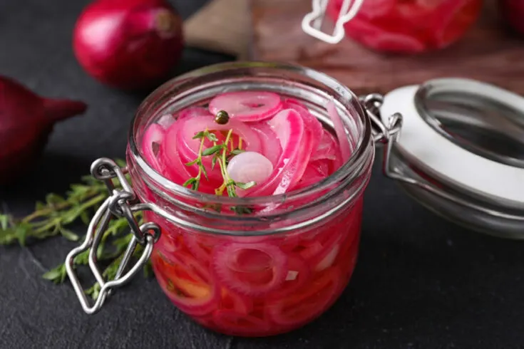 A jar of pickled red onions on a dark background