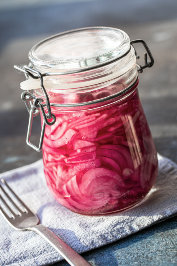 A jar of pickled red onions sitting on a white napkin and a fork nearby.