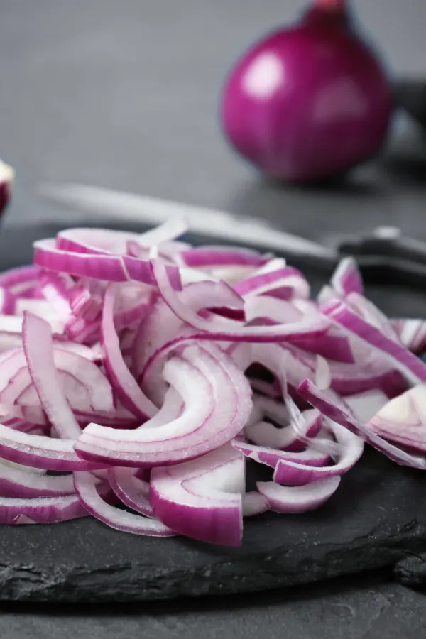 A pile of sliced onions on a black slate.